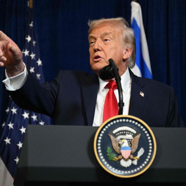 Donald Trump gestikuliert an einem Rednerpult mit dem US-amerikanischen Wappen.