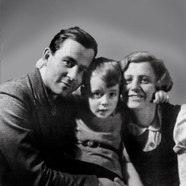 Ein Mann, ein Kind und eine Frau sitzen eng beieinander und lächeln gemeinsam in die Kamera.