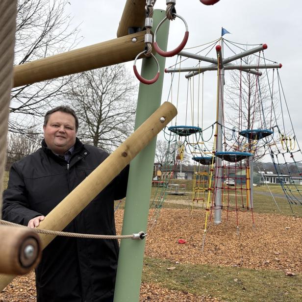 Ein Mann in Jacke steht auf einem Spielplatz mit Klettergerüsten.