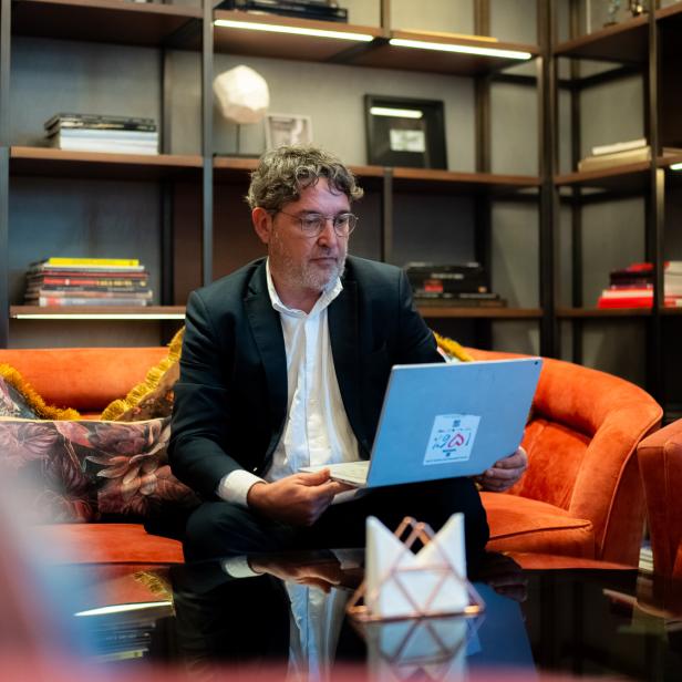 Mann im Anzug arbeitet mit Laptop auf orangefarbenem Sofa vor Bücherregal.