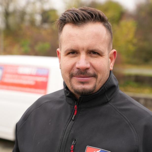 Ein Mann steht draußen. Man sieht nur seinen Kopf und seine Brust. 