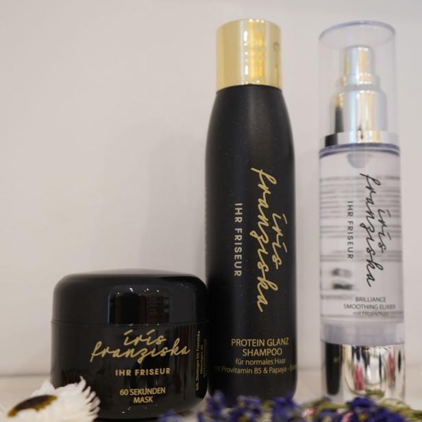 Drei Haarpflegeprodukte von Iris Franziska – Ihr Friseur, umgeben von Trockenblumen.