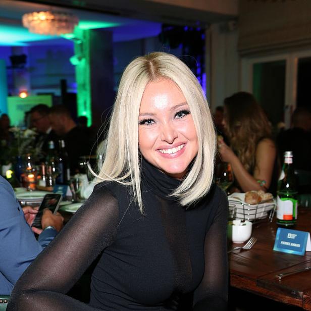 Patrice Aminati sitzt lächelnd an einem festlich gedeckten Tisch bei einer Veranstaltung.