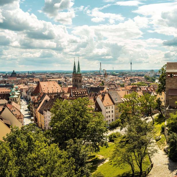 Blick über die Altstadt von Nürnberg mit historischen Gebäuden, Türmen und grünen Bäumen unter bewölktem Himmel