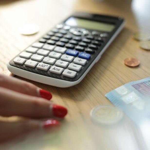 Taschenrechner, Geldscheine und Münzen und eine weibliche Hand