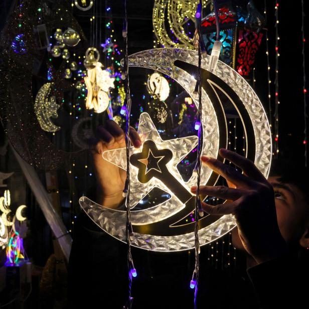 Eine Person hält eine leuchtende Dekoration in Form von Halbmond und Stern zwischen bunten Lichterketten.