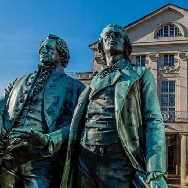 Zwei Statuen von Goethe und Schiller vor einem historischen Gebäude in Weimar.