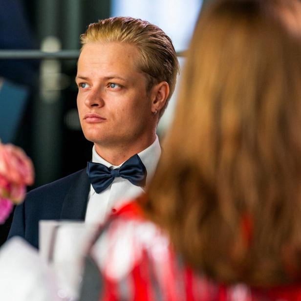 Marius Borg Høiby im Anzug mit Fliege sitzt an einem festlich gedeckten Tisch mit Blumen und schaut nach vorne.