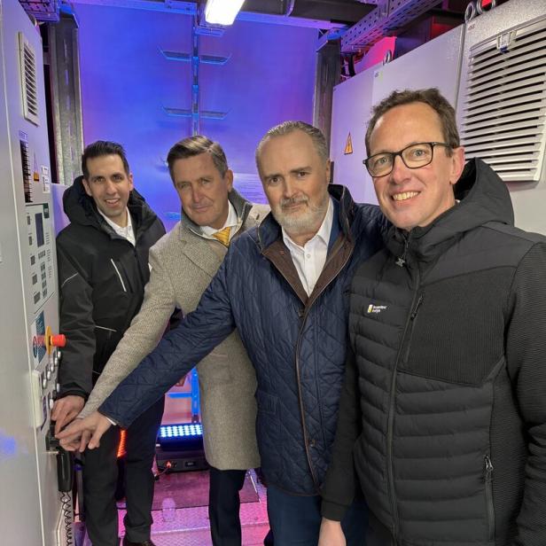 Vier Männer stehen in einem Raum mit technischer Ausrüstung und bedienen gemeinsam eine Steuerung.