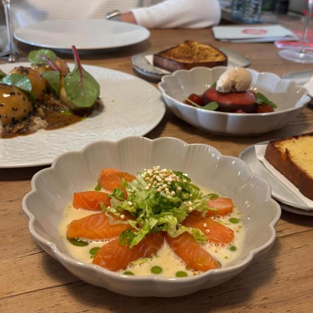 Eine Aufnahme von einem Esstisch auf dem mehrere Speisen stehen, darunter Lachs, Knödl und Brioche.