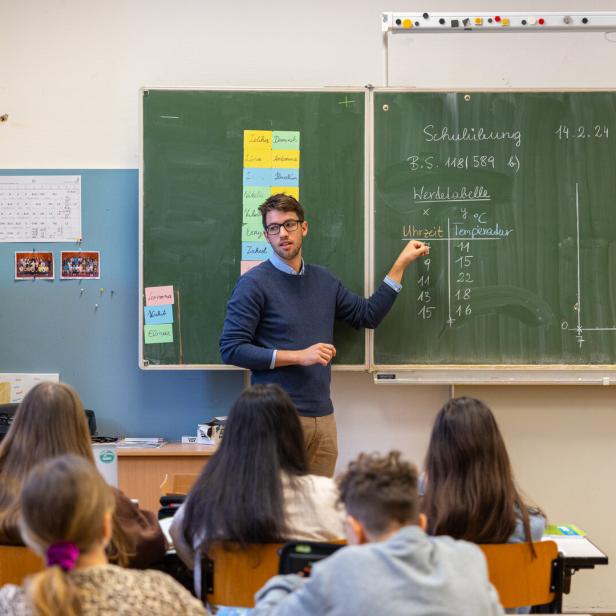 Ein Lehrer erklärt vor einer Klasse eine Wertetabelle mit Uhrzeiten und Temperaturen an der Tafel.