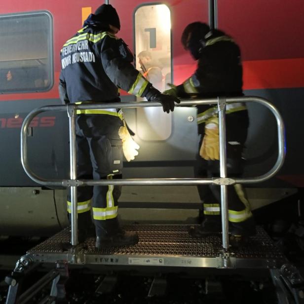 Zwei Feuerwehrleute stehen nachts auf einer mobilen Plattform vor einem Zug.