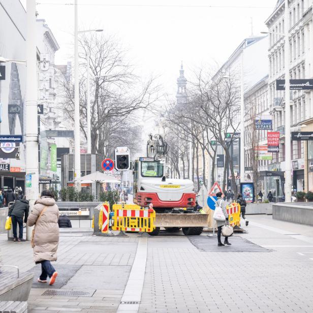 Eine Baustelle mit Bagger blockiert eine Straße in Wien, im Hintergrund ist die Votivkirche sichtbar.