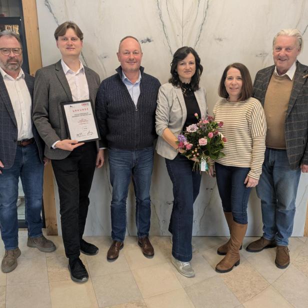 Sechs Personen stehen nebeneinander, eine Person hält eine Urkunde, eine andere einen Blumenstrauß.