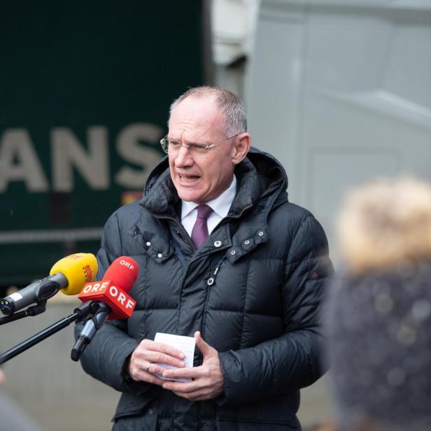 Ein Mann spricht bei einer Pressekonferenz im Freien neben einem Polizisten.
