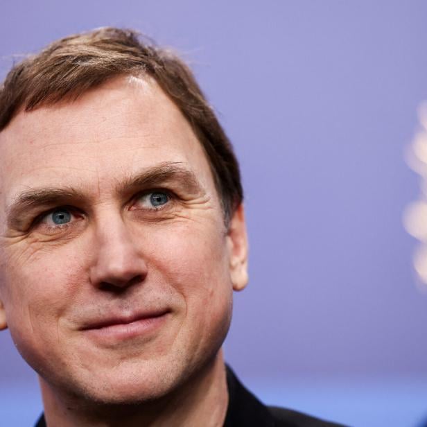 Lars Eidinger mit hellbraunen Haaren und blauen Augen blickt lächelnd nach oben.