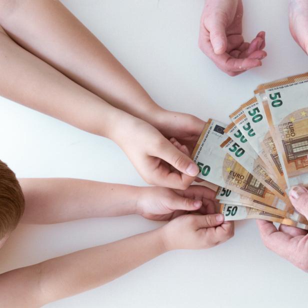 Ein Kind und eine ältere Person halten gemeinsam einen Fächer aus 50-Euro-Scheinen.