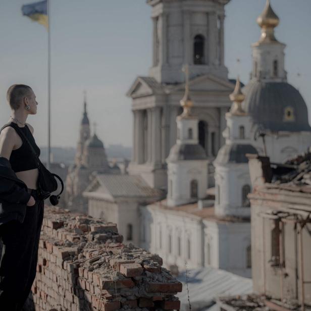 Eine Frau auf einem Dach schaut auf ein zerstörtes Gebäude