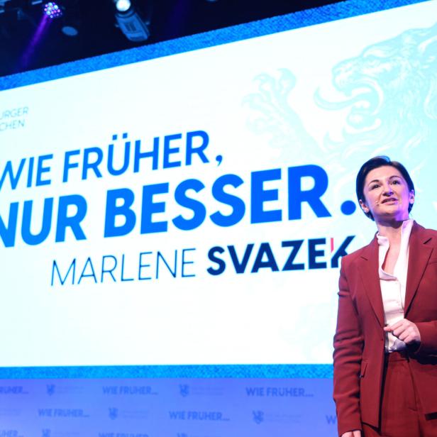 Eine Frau im roten Anzug steht auf einer Bühne vor einer großen Leinwand mit dem Slogan „Wie früher, nur besser.“