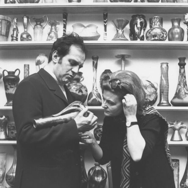 Ein Mann und eine Frau (Otto und Renee Schenk) betrachten eine Vase vor einem Regal voller Vasen.