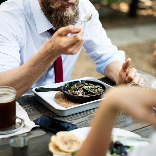 Zwei Personen essen gemeinsam an einem Holztisch im Freien verschiedene Gerichte.