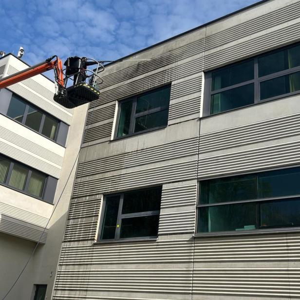 Fassadenreinigung eines modernen Bürogebäudes mit Hebebühne bei sonnigem Wetter.