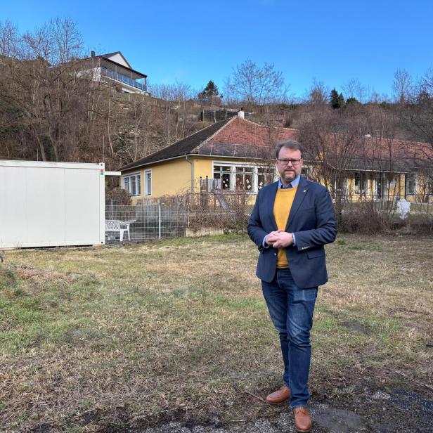 Florian Kamleitner steht vor dem Kindergarten und einer Containerklasse auf einer braun-grünen Wiese.