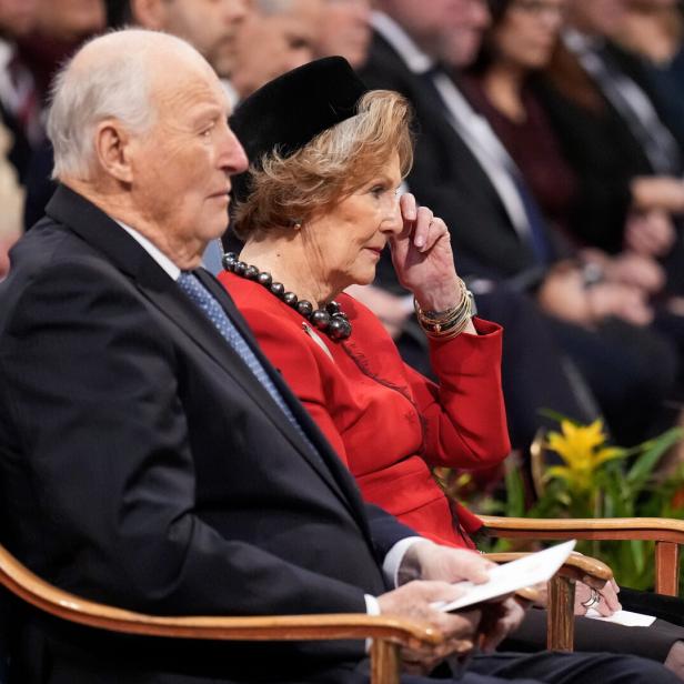 König Harald V. und Königin Sonja sitzen in einer Menschenmenge.