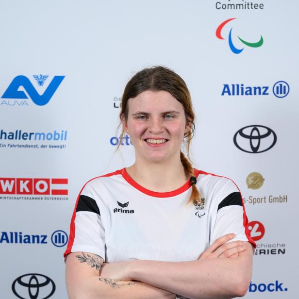 Veronika Aigner: Junge Frau mit verschränkten Armen im Sporttrikot steht vor einer Sponsorenwand und lächelt.