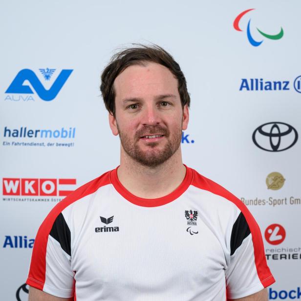 Thomas Grochar: Ein Mann mit kurzem Bart trägt ein weiß-rotes Sporttrikot mit österreichischem Wappen und steht vor einer Sponsorenwand.