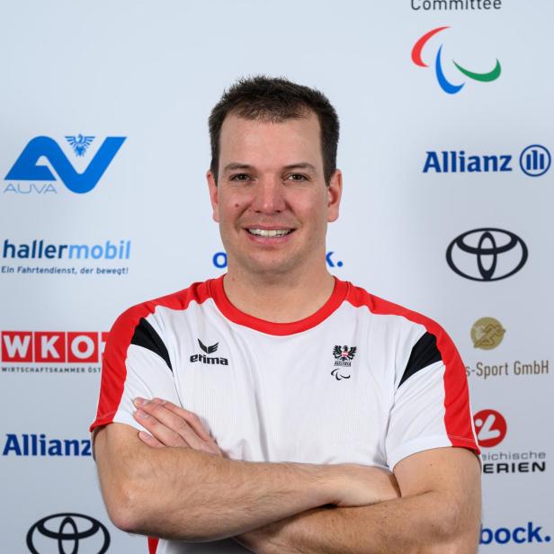 Markus Salcher: Ein Mann mit kurzem Haar trägt ein rot-weißes Sporttrikot und steht mit verschränkten Armen vor einer Sponsorenwand.