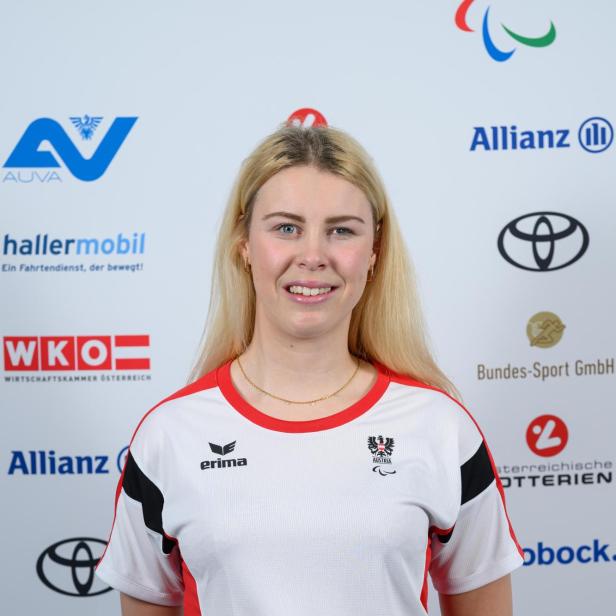 Laura Streng : Junge Frau mit langen blonden Haaren trägt ein österreichisches Sporttrikot und steht vor einer Sponsorenwand.