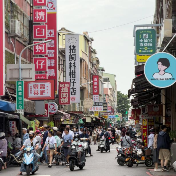Eine belebte Straße in Taiwan mit vielen Menschen, Rollern und bunten Schildern