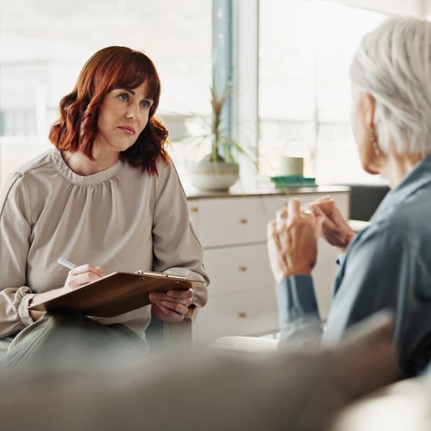 Zwei Frauen sitzen sich in einem modernen Raum gegenüber, eine macht sich Notizen, während die andere spricht.