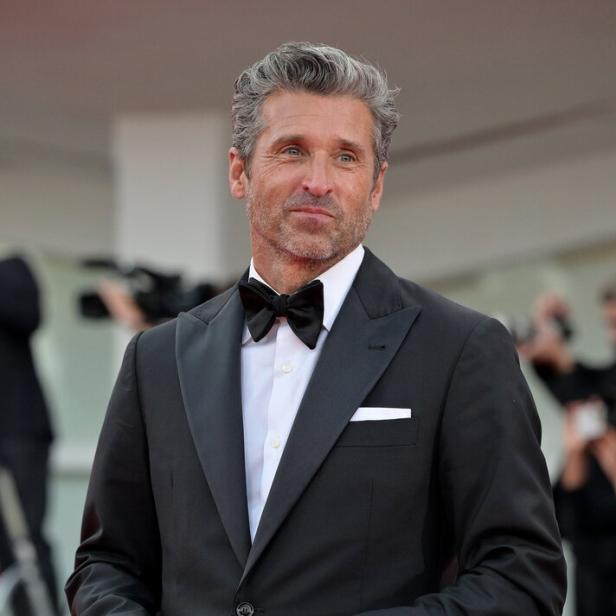 Patrick Dempsey trägt einen schwarzen Smoking mit Fliege und hält eine Brille in der Hand.
