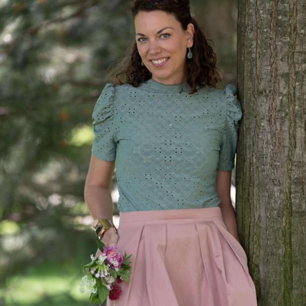 Katalin Kardos lehnt an einem Baum und hält Blumen in der Hand