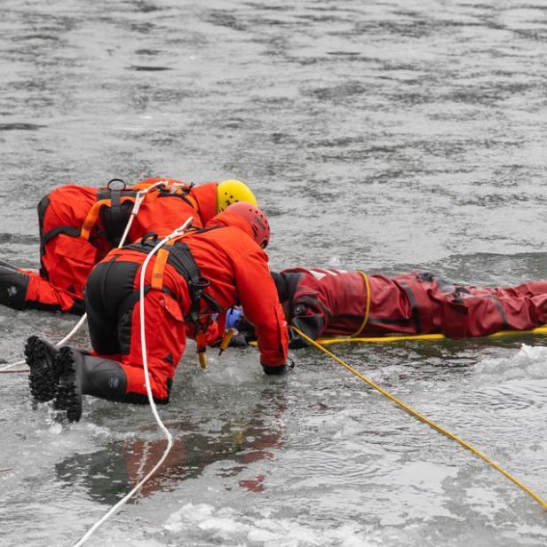Zwei Feuerwehrmänner ziehen eine Person aus dem Eis.