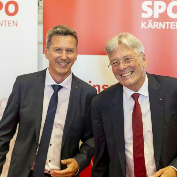 Zwei lächelnde Männer in Anzügen stehen vor einem SPÖ Kärnten Banner.