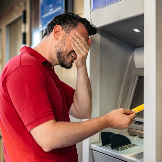 Mid-Adult Man Covering His Eyes Before Withdrawing Money Using A Credit Card At The ATM Machine