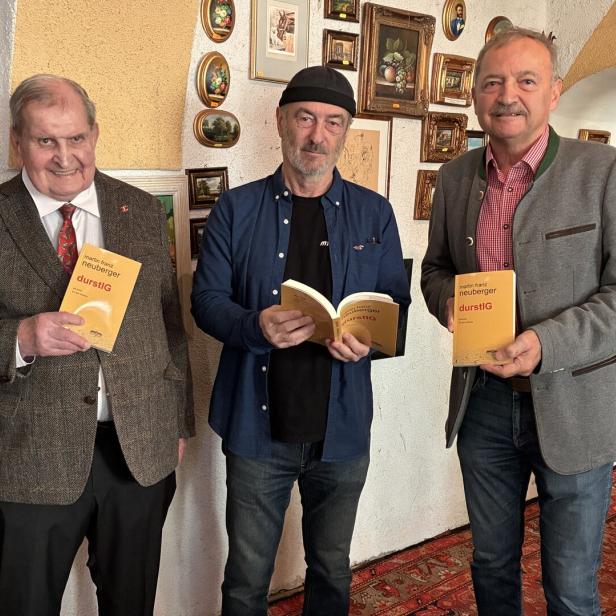 Drei Männer präsentieren das Buch "durstIG" von Martin Franz Neuberger vor einer Wand mit Bildern.