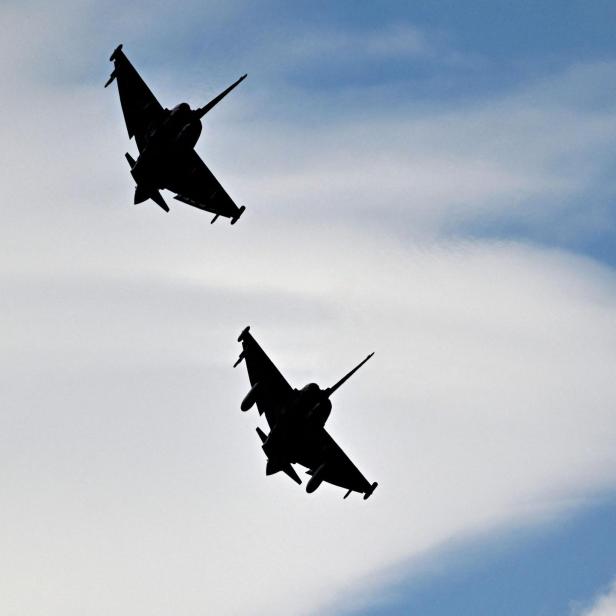 Zwei Kampfjets fliegen nebeneinander am Himmel vor weißen Wolken.