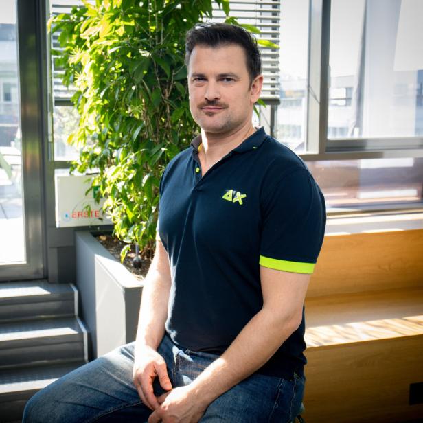 Ein Mann sitzt in einem modernen, sonnendurchfluteten Raum neben einer großen grünen Pflanze.