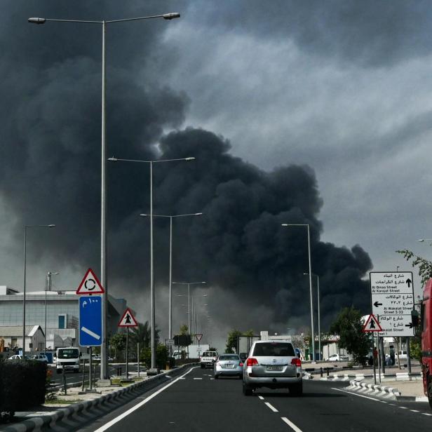 Dichter, dunkler Rauch steigt über einer Straße mit Autos und Straßenschildern auf.
