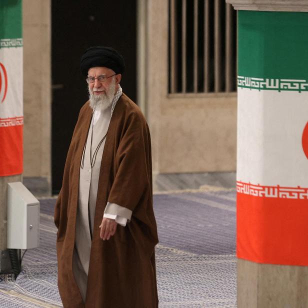 Ali Khamenei geht an Säulen mit iranischen Flaggen vorbei.