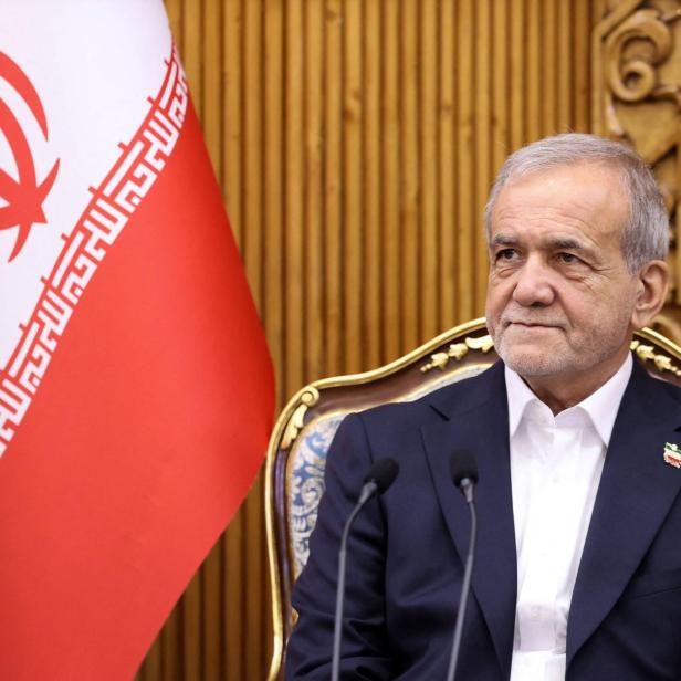 Ein Mann im Anzug sitzt neben der iranischen Flagge.