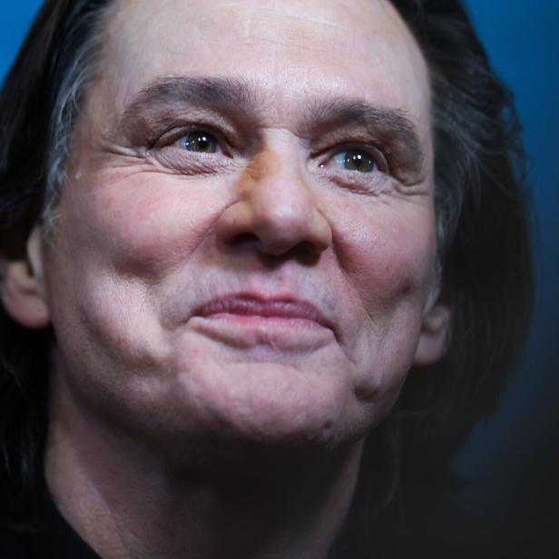 Eine Person mit mittellangen dunklen Haaren lächelt leicht vor blauem Hintergrund.