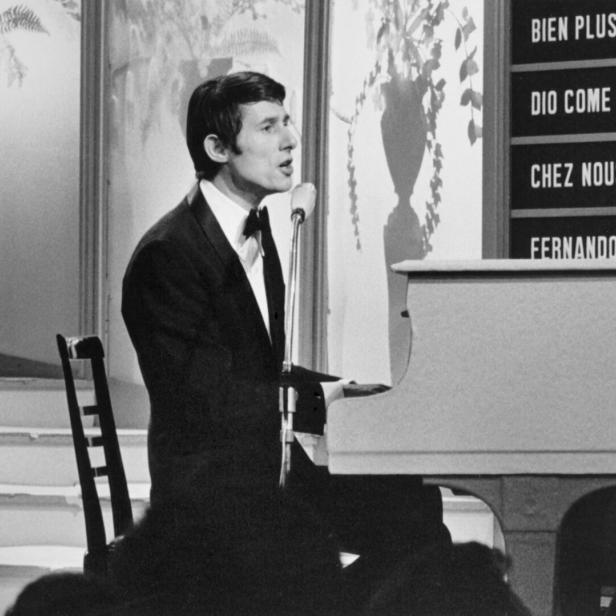 Ein Sänger mit Anzug und Fliege steht am Klavier und singt ins Mikrofon.