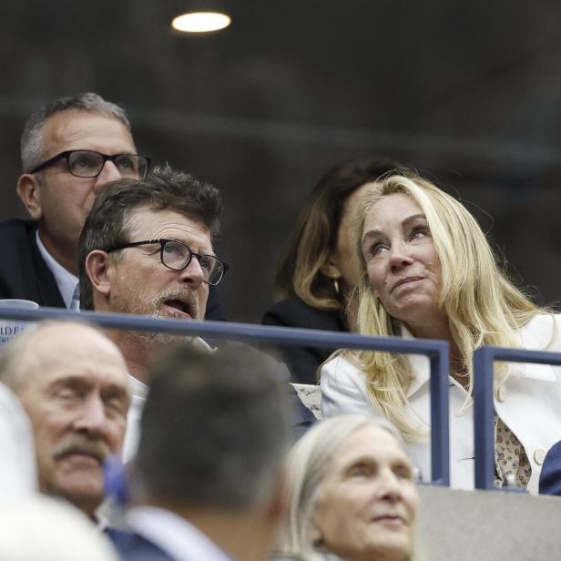 Michael J. Fox und Tracy Pollan sitzen nebeneinander auf einer Tribüne und schauen aufmerksam in eine Richtung.