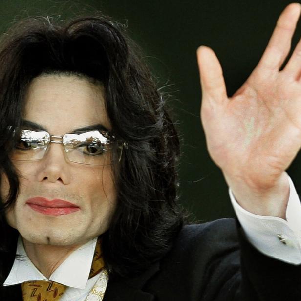 Michael Jackson mit Brille und Anzug winkt in die Kamera.