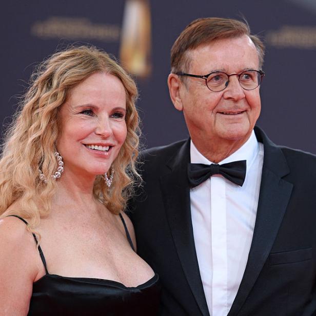 Hans Mahr mit Fliege und Moderatorin Katja Burkard mit blonden Locken lächeln auf einem Event.